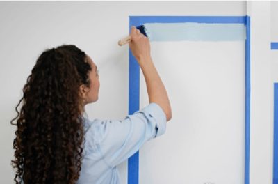 A person painting an edge along a strip of blue painter's tape.