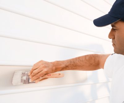 A person painting siding with a brush.