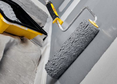 A Purdy roller applying gray paint to a wall.