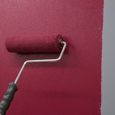 Applying red paint to a wall with a roller.