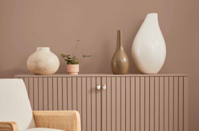 Wall painted Sherwin-Williams Redend Point SW9081 with three beige ceramic art vases sitting on a wood accent cabinet.