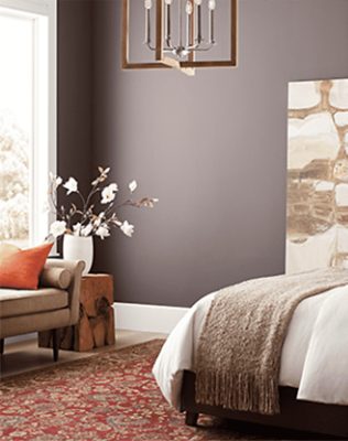 Dark purple walls with edge of bed, loveseat, and some decor in frame,.