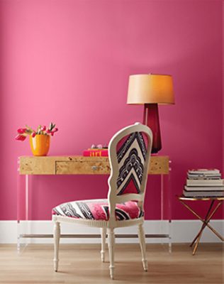 Pink walls with wooden desk and lamp and printed desk chair..