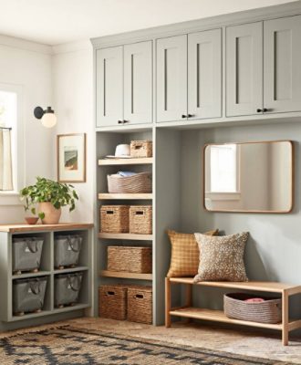 A multi-purpose room with many greenish gray shelves and overhead cabinets above a wooden bench and mirror.