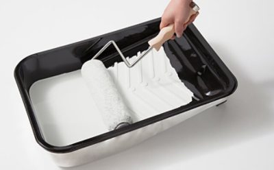 A paint tray with white paint and a paint brush