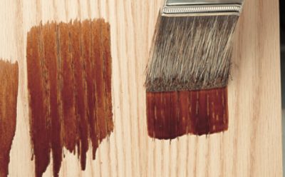 Applying stains to a piece of wood with a brush.