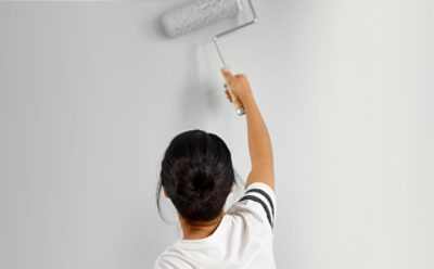A person painting a white wall with a paint roller. 