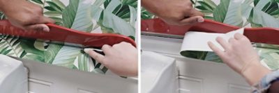 Two people remove excess tropical green wallpaper from their bathroom walls.