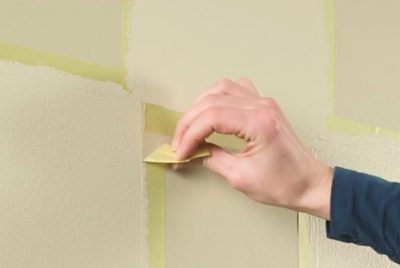 Hand removing tape from a painted wall.