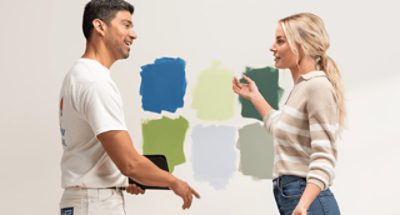 Two people talking in front of a wall with six different paint color samples.