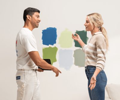 Two people talking in front of a wall with six different paint color samples.