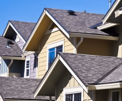A house exterior painted tan with a gray house in the background.