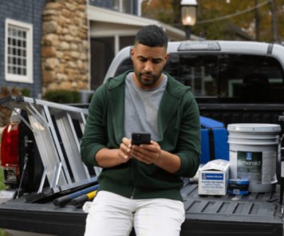 A person sitting in the back of a truck on his phone with paint supplies in the background.