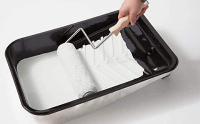 A paint tray with white paint and a roller. 