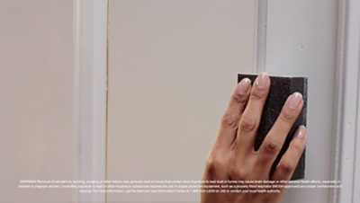 A woman sanding a door to remove paint buildup.