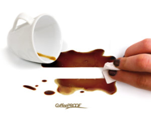 Hand cleaning spilled coffee from a white surface with a cloth.