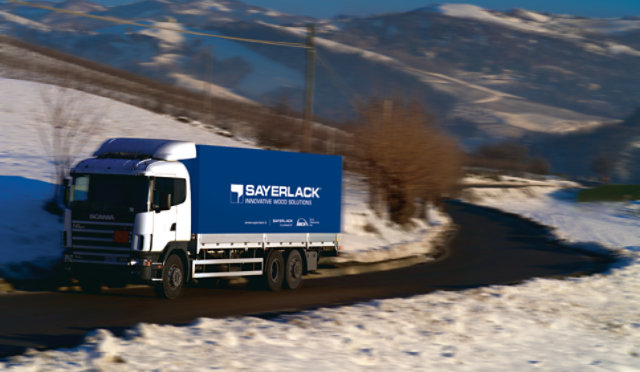 Sayerlack truck driving through a snowy mountain landscape with 'Innovative Wood Solutions' on the container.