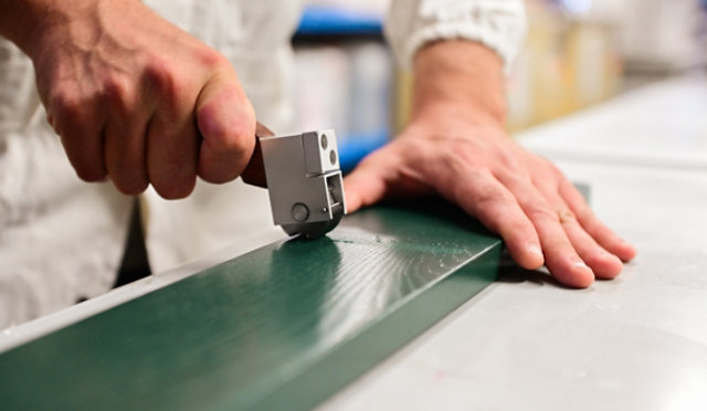 Hand applying a coating quality test on a green wooden panel.