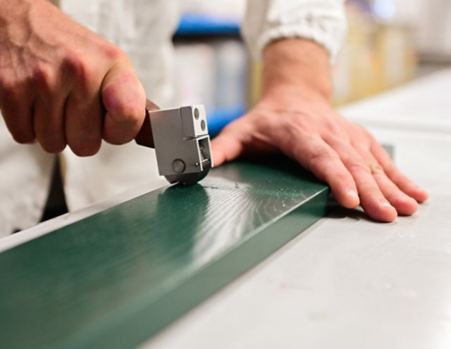 Hand applying a coating quality test on a green wooden panel.