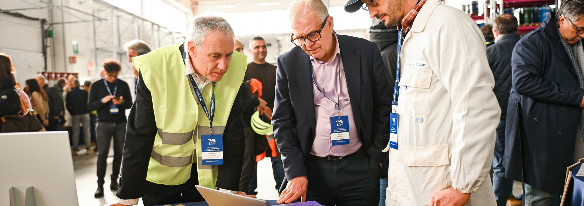 Three people reviewing wood samples and a laptop during Sayerlack’s 70th anniversary event in a warehouse setting.