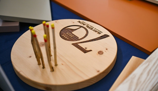 Wooden display piece engraved with Sayerlack 70th anniversary logo, surrounded by color samples.