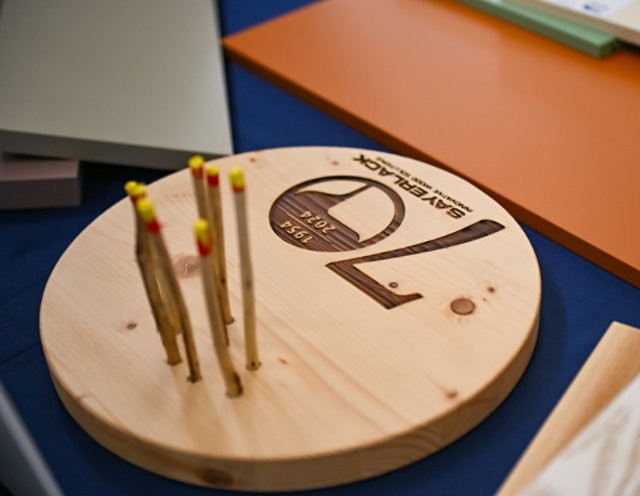 Wooden display piece engraved with Sayerlack 70th anniversary logo, surrounded by color samples.