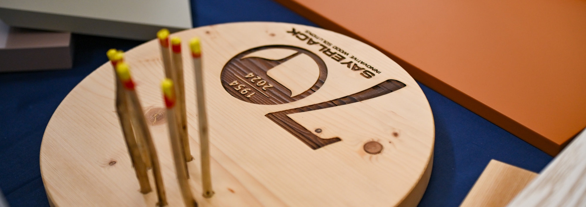 Wooden display piece engraved with Sayerlack 70th anniversary logo, surrounded by color samples.