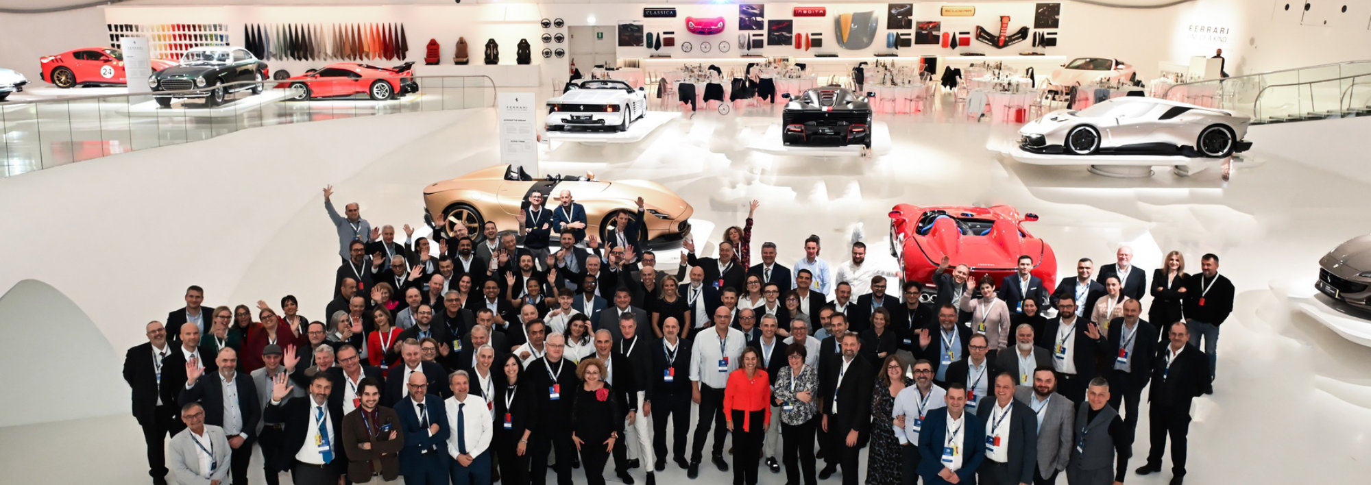 Large group photo at an automotive showroom with sports cars in the background.