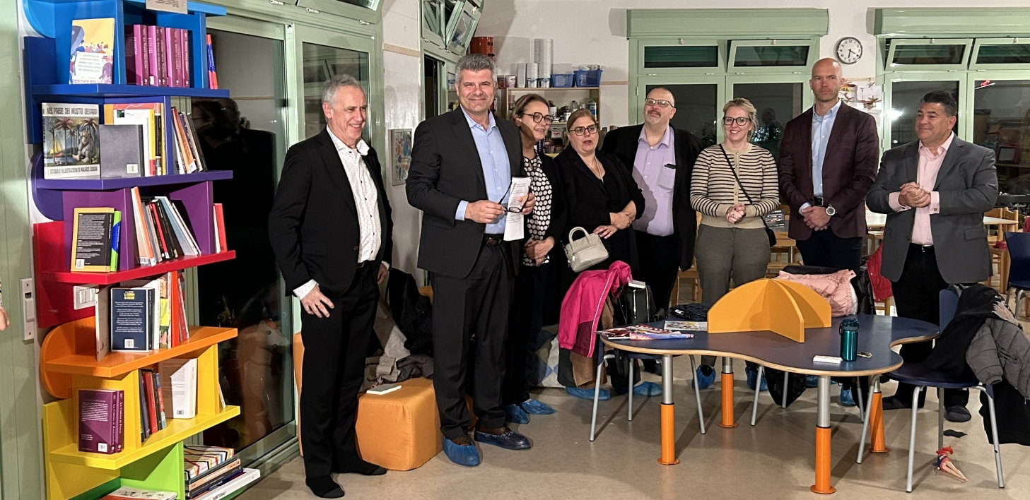 Group of people standing in a colorful classroom with bookshelves and tables.