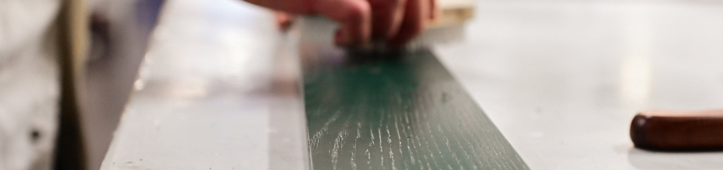 Hand applying or refining a coating on a green wooden surface with visible grain, in a laboratory