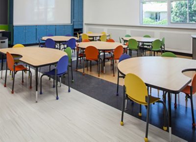 A brightly lit classroom with tables and colorful chairs.