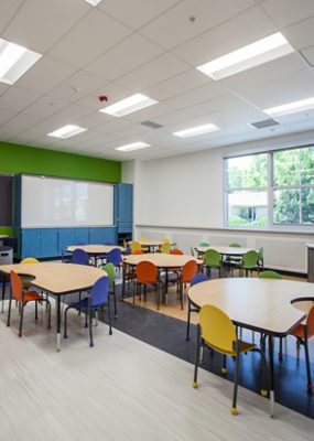 A brightly lit classroom with tables and colorful chairs.