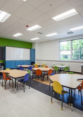 A brightly lit classroom with tables and colorful chairs.