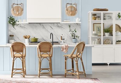 Kitchen with walls and island painted in the Sherwin-Williams Color of the Year, Upward, with rattan chairs, a white marble backsplash, and white cabinet displaying serving pieces and decorative accents.