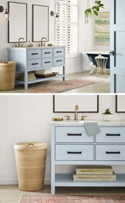 Modern primary bathroom with white walls and light blue double vanity with shuttered window, hanging plants, rattan hamper and navy blue clawfoot tub.