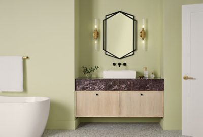 A modern bathroom featuring a freestanding white bathtub, a door painted White Flour, a Pickled Oak vanity with a dark marble countertop, a hexagonal, black-framed mirror, and sconces set against Celery walls.