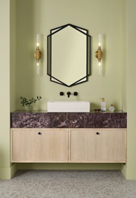 A modern bathroom featuring a freestanding white bathtub, a door painted White Flour, a Pickled Oak vanity with a dark marble countertop, a hexagonal, black-framed mirror, and sconces set against Celery walls.