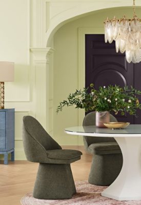 A luxurious dining room featuring Celery walls and Plum Brown double doors, a round white table with upholstered chairs, a blue sideboard with a lamp, and an ornate chandelier overhead.