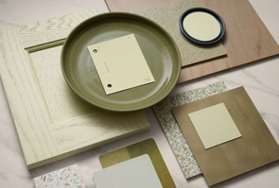 A collection of design samples including a green plate with a Celery color chip, wood panels, and various materials arranged on a marble surface.