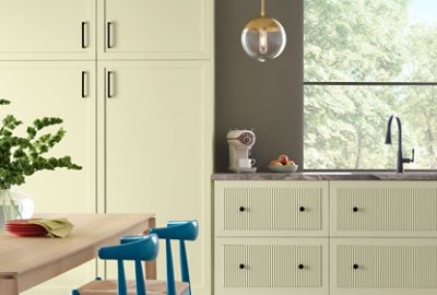 A modern kitchen featuring Celery cabinets, Cocoon walls, a gray marble countertop with an espresso maker and fruit bowl, and Georgian Bay chairs at a wooden dining table with a vase of green plants.