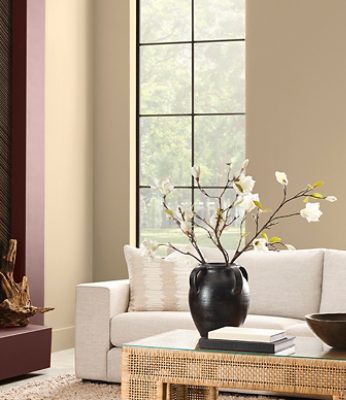 Modern living room with Universal Khaki walls, Dark Auburn painted fireplace, beige sofa, dark vase with flowers, and a glass-topped coffee table. 
