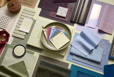 A variety of fabric samples and color swatches arranged on surface, featuring a green plate in the center with color samples of all the coordinating hues for this year’s Color of the Year: Plum Brown, Woven Wicker, Kirsch Red, White Flour, Cocoon, Potentially Purple, Georgian Bay, Cosmos, Artichoke, and Celery.