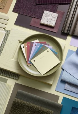 A variety of fabric samples and color swatches arranged on surface, featuring a green plate in the center with color samples of all the coordinating hues for this year’s Color of the Year: Plum Brown, Woven Wicker, Kirsch Red, White Flour, Cocoon, Potentially Purple, Georgian Bay, Cosmos, Artichoke, and Celery.