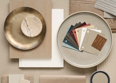 Flat lay of interior design materials including color swatches, a marble piece, brass dish, textile samples, and wood samples. 