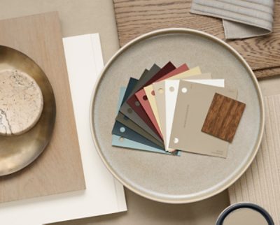 Flatlay featuring a ceramic plate with paint swatches of Universal Khaki and its coordinating colors alongside design materials on a neutral surface. 