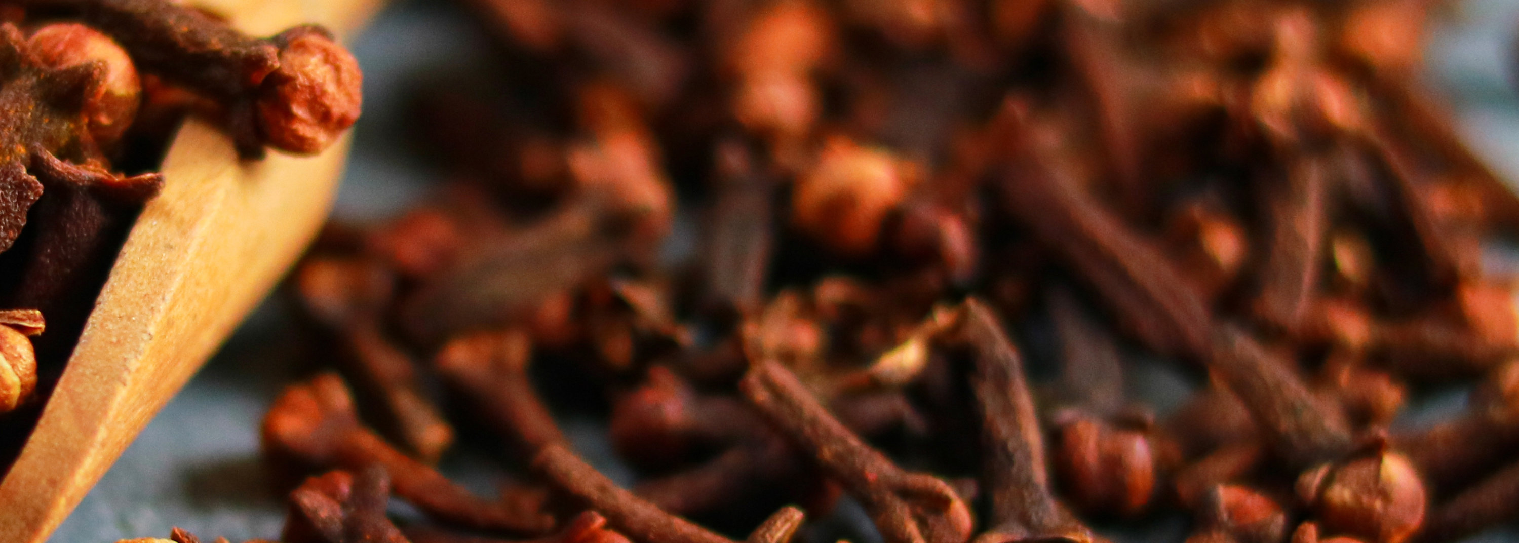 Spices cloves in a wooden spoon on a blue background. Close-up