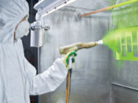 Technician spraying green powder on piece of equipment 