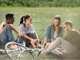 4 people sitting around a bike in a field with canned drinks