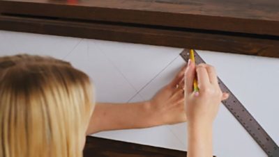 A woman is sketching a new design with a pencil and ruler on the dresser drawer.