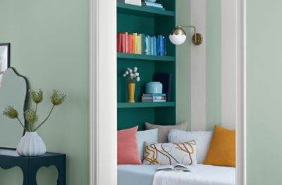 Looking into a sitting area with a bookshelf and walls painted vertical stripes of Slow Green SW 6456 and an off-white.